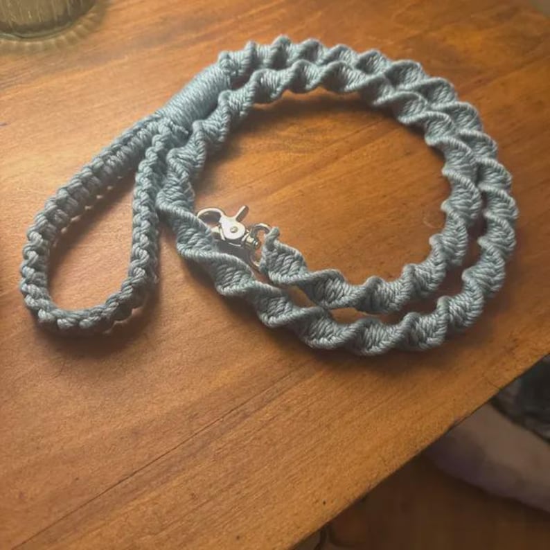 Puede incluir: Una correa de macram&eacute; azul claro que presenta un patr&oacute;n de nudos en espiral a lo largo de toda la cuerda. La correa incluye un asa en un extremo y un mosquet&oacute;n giratorio de metal de tono plateado en el otro para una sujeci&oacute;n segura.