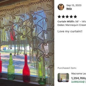 May include: A cream-colored macrame window curtain featuring a leaf pattern and fringe, measuring 56 inches in width. The curtain hangs in front of a window with several green and red glass bottles placed on the wooden windowsill below.