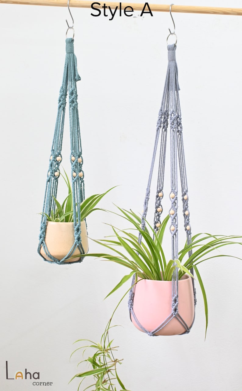 May include: Two macrame plant hangers, one in light blue and one in gray, with wooden beads. Each hanger is holding a potted plant.
