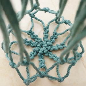 Pu&ograve; includere: Un portavasi sospeso in macram&egrave; blu-verde con un motivo a stella. Il macram&egrave; &egrave; realizzato con una corda spessa e presenta un design annodato.