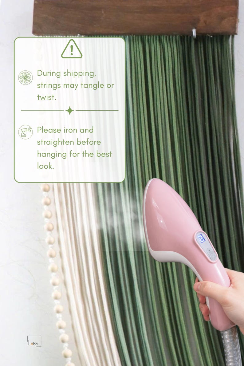 May include: A handheld pink garment steamer emitting steam onto a wall hanging made of long, vertical green and cream-coloured strings attached to a wooden bar. A white informational box with green text advises to iron and straighten strings.