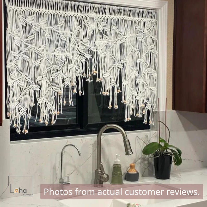 May include: A white macrame window valance featuring a knotted leaf pattern and hanging fringe with small wooden beads at the ends. The valance is suspended across the top of a window frame, displaying intricate cord work and a textured design.