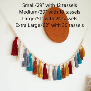May include: A wooden bead garland with colorful tassels in red, white, gray, teal, orange, and yellow. The garland is 62 inches long and has 30 tassels. Various sizes are available: Small (29 inches, 12 tassels), Medium (39 inches, 18 tassels), Large (51 inches, 24 tassels).