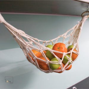Pode incluir: Uma rede de corda de algodão branco pendurada no teto, cheia de limas verdes e tangerinas laranja.