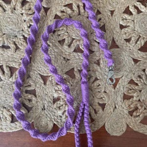 Puede incluir: Un cord&oacute;n de color morado elaborado con un patr&oacute;n de nudos de macram&eacute; en espiral. El cord&oacute;n cuenta con un mosquet&oacute;n giratorio de metal plateado en un extremo, dise&ntilde;ado para sujetar objetos de forma segura. Hecho de fibra anudada.