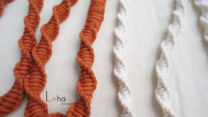 Puede incluir: Dos juegos de cordones de macram&eacute; trenzados, uno en un color naranja quemado intenso y otro en un color crema blanquecino. Los cordones presentan un patr&oacute;n repetitivo de nudos en espiral a lo largo de su longitud. El texto Laha corner est&aacute; impreso.