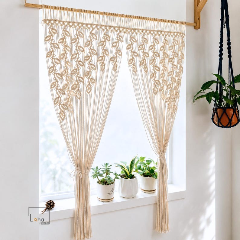 May include: A cream-colored macrame curtain featuring a repeating leaf-like knot pattern, suspended from a wooden rod. The curtain is divided into two panels, each gathered with a tie, and displays the Laha Corner logo in the bottom left corner.