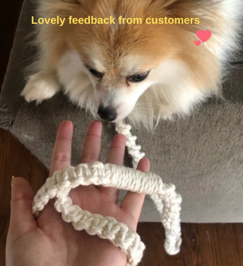 Puede incluir: Una correa de macram&eacute; de color crema con textura anudada sostenida en una mano, con un peque&ntilde;o perro esponjoso mirando hacia la correa. El texto "Lovely feedback from customers" est&aacute; impreso en amarillo en la parte superior con un icono de coraz&oacute;n rosa.