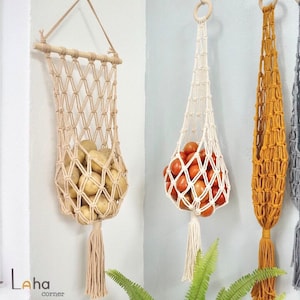 May include: Four macrame hanging baskets in beige, cream, mustard yellow, and gray. The baskets feature a knotted net design with a tassel at the bottom. The first basket holds potatoes, the second holds tomatoes, and the others are empty.