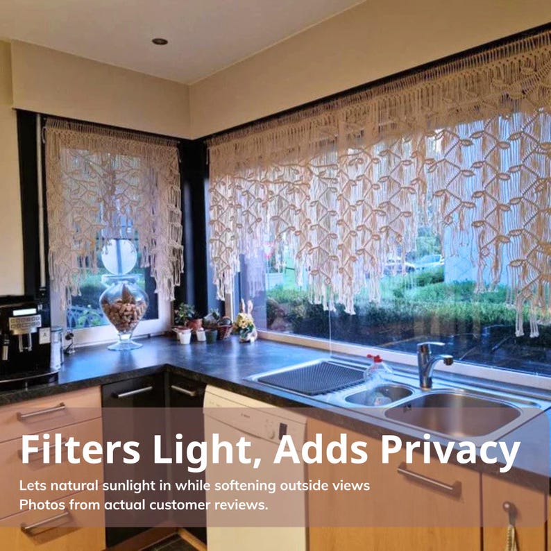 May include: Off-white macrame window valance featuring an intricate knotted pattern with hanging fringe, installed over a kitchen window. The textile displays a decorative weave that filters light while maintaining privacy for the interior space.
