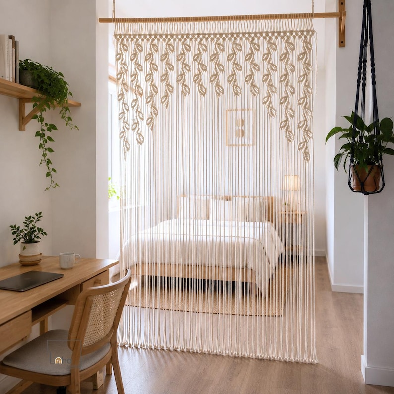 May include: A cream-colored macrame room divider featuring a series of knotted leaf-shaped patterns along the top edge, suspended from a horizontal wooden rod. The long, vertical cords hang down to create a textured, semi-transparent partition.