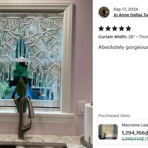 May include: A bright white macrame window curtain featuring a knotted leaf pattern with long, loose fringe hanging from a rod. The curtain measures 28 inches in width and is displayed covering a window pane, showcasing intricate fiber art knots.