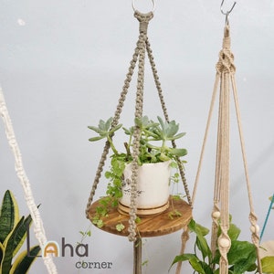 May include: Three macrame plant hangers with wooden shelves. The hangers are made with white, beige, and turquoise cord. The shelves are holding potted plants.