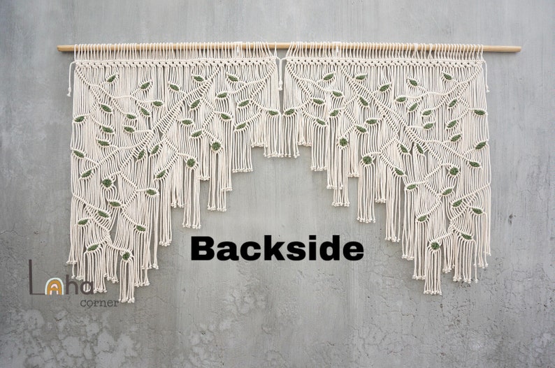 May include: A macrame wall hanging featuring off-white cotton cord knotted into a branch and leaf pattern with small dark green accents. The piece is suspended from a horizontal wooden dowel and includes the text Backside and Laha corner.
