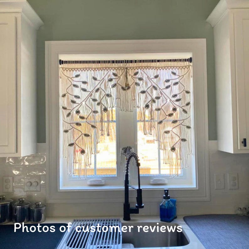 May include: A cream-colored macrame window valance featuring an intricate leaf-like pattern with knotted fringe details. The textile hanging is suspended from a dark rod and displays a symmetrical design of woven cord loops and vertical strands.