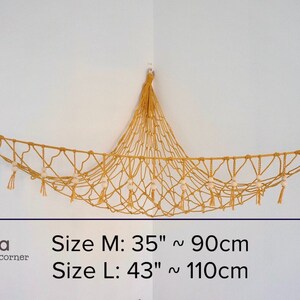 May include: A macrame hammock with wooden beads and tassels hanging from the ceiling. The hammock is made of natural beige rope and is 35 inches or 90 centimeters long. The hammock is labeled "Size M: 35" ~ 90cm" and "Size L: 43" ~ 110cm".