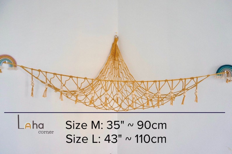 May include: A macrame hammock with wooden beads and tassels hanging from the ceiling. The hammock is made of natural beige rope and is 35 inches or 90 centimeters long. The hammock is labeled "Size M: 35" ~ 90cm" and "Size L: 43" ~ 110cm".