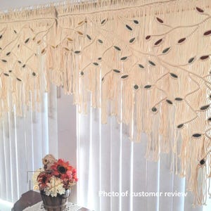 May include: A cream-colored macrame window valance featuring an intricate knotted branch design with embedded leaf-shaped accents in shades of brown, green, and gold. The piece includes long, hanging fringe strands and a top rod pocket.