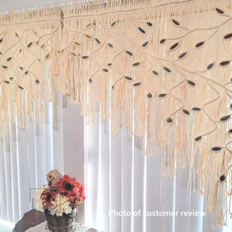 May include: A cream-colored macrame window valance featuring an intricate knotted branch design with embedded leaf-shaped accents in shades of brown, green, and gold. The piece includes long, hanging fringe strands and a top rod pocket.