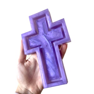 Puede incluir: Una cruz grande de color púrpura hecha de resina con un acabado brillante. La cruz es hueca y tiene un diseño en relieve.