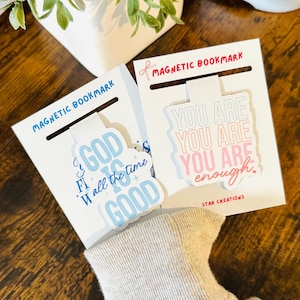 May include: Two white magnetic bookmarks with inspirational quotes. One bookmark reads "God is good all the time" in blue, and the other says "You are enough" in pink and gray. Both have "Magnetic Bookmark" printed at the top.
