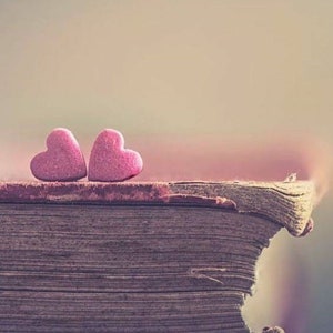 May include: Two pink heart-shaped candies on top of a worn, brown book.