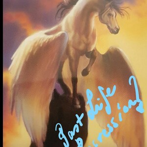 May include: A white winged horse with a black mane and tail stands on a rock against a sunset background. The words "past life regressions" are written in blue on the image.