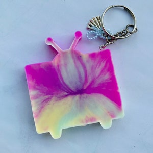 May include: A pink and yellow tie-dye television keychain with a silver key ring and charm.