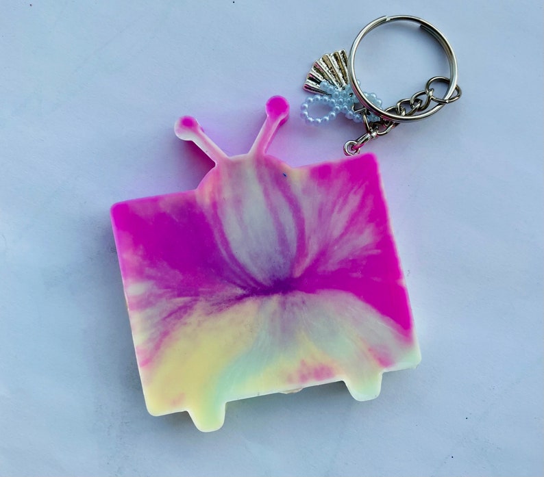 May include: A pink and yellow tie-dye television keychain with a silver key ring and charm.