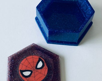 May include: A blue glitter hexagonal box with a lid featuring a red and black Spider-Man logo on a purple glitter background.
