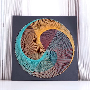 May include: A circular string art piece with a black background. The string art is made with turquoise, orange, and red thread, creating a geometric design.