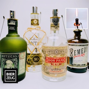 May include: Four glass liquor bottles repurposed as oil lamps, each featuring a metal wick holder and a small metal cap on a chain. The bottles include labels for Botucal, Plantation XO, Don Papa, and Remedy Spiced Rum. One inset shows a lit wick.