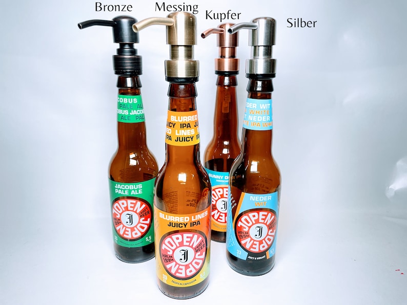 May include: Four glass bottles with different coloured labels and pump tops. The labels have text in Dutch and English. The pump tops are bronze, brass, copper, and silver.