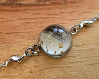 May include: A silver bracelet with a round, clear glass charm containing strands of hair and gold flakes.