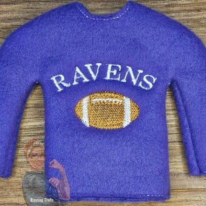 May include: Purple felt elf shirt with the word "RAVENS" and a white and gold football design.