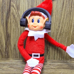 May include: A red and white striped elf doll wearing a red hat with a white tip, a white collar, and a black belt. The elf has a smiling face, blue eyes, and is wearing black headphones.