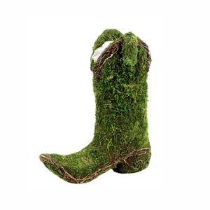 May include: A decorative cowboy boot covered in vibrant green moss. The boot features a pointed toe and is accented with natural-looking twigs and a white interior. This unique piece adds a touch of rustic charm to any space.