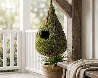 May include: A hanging teardrop-shaped birdhouse covered in green moss, with a small round opening. The birdhouse is suspended from a wooden beam. A terracotta pot with a fern and a wooden bench are in the background.