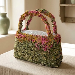 May include: A decorative handbag made of woven green grass, decorated with pink and yellow dried flowers. The handles are also decorated with flowers. The bag has a rectangular shape and a clear plastic liner inside.