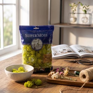 May include: A bag of SuperMoss reindeer moss, a decorative item for home and garden use. The bag is blue and clear, filled with bright green moss. A small white bowl with moss, dried flowers, and twine are also on the wooden table.