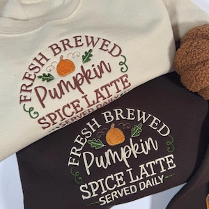 May include: Two sweatshirts with embroidered text that reads "Fresh Brewed Pumpkin Spice Latte Served Daily". One sweatshirt is beige and the other is brown.