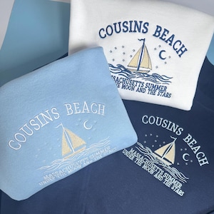 Peut inclure: Trois sweatshirts blancs, bleu clair et bleu marine, chacun brodé avec "COUSINS BEACH" au-dessus d'un motif de voilier. Le texte "MASSACHUSETTS SUMMER UNDER THE MOON AND THE STARS" est également brodé sur chaque sweat-shirt.