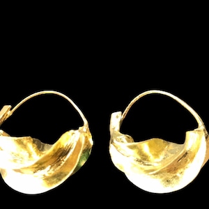 May include: A pair of gold hoop earrings with a wavy, organic design. The earrings are made of a smooth, shiny metal.
