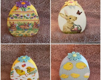 May include: Four wooden Easter egg-shaped boxes decorated with different spring-themed designs. The boxes are yellow, blue, and white with floral accents and images of bunnies, chicks, and flowers.