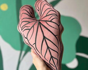 Può includere: Un cuscino di velluto rosa a forma di foglia con venature ricamate in verde scuro.