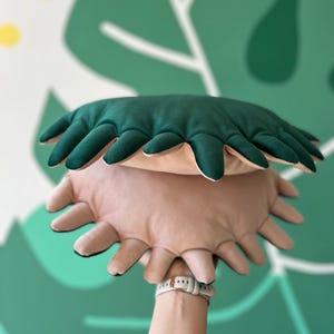 Puede incluir: Una almohada de felpa verde y beige con un diseño único de borde festoneado. La almohada tiene forma de flor con múltiples pétalos.