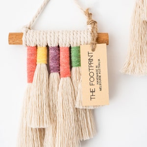 Close up view of the product tag of a rainbow macrame wall hanging. Tag reads, The Footprint - Handmade in Melbourne Australia.