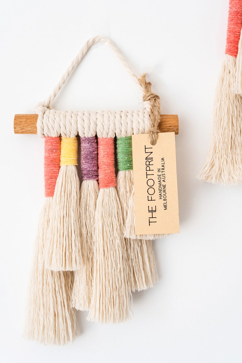 Close up view of the product tag of a rainbow macrame wall hanging. Tag reads, The Footprint - Handmade in Melbourne Australia.