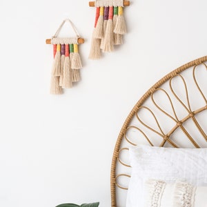 Two rainbow macrame wall hangings hanged above a bed in a kids bedroom.