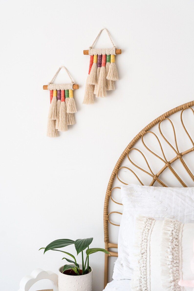 Two rainbow macrame wall hangings hanged above a bed in a kids bedroom.